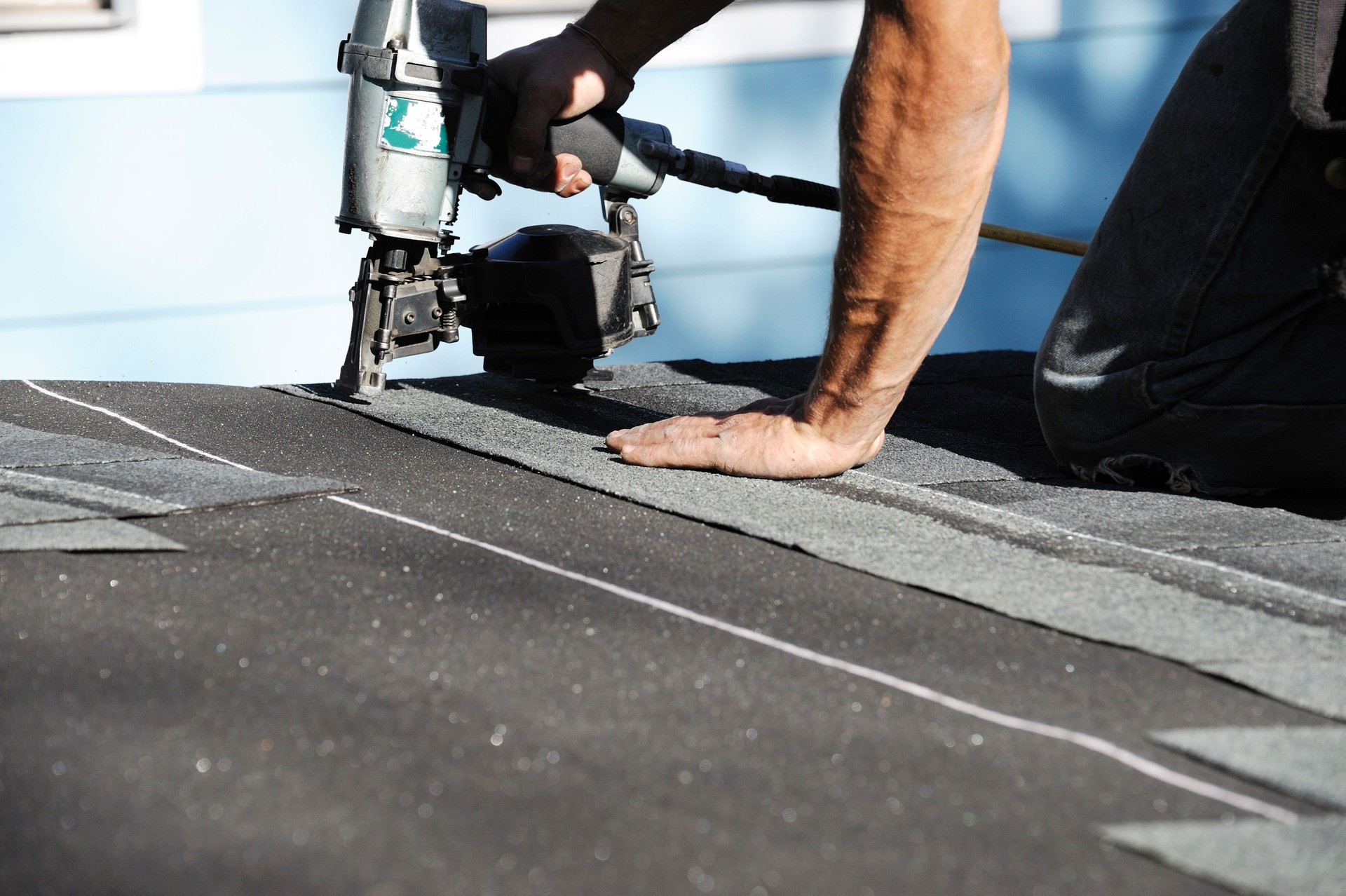 handyman using nail gun to install shingle to repair roof