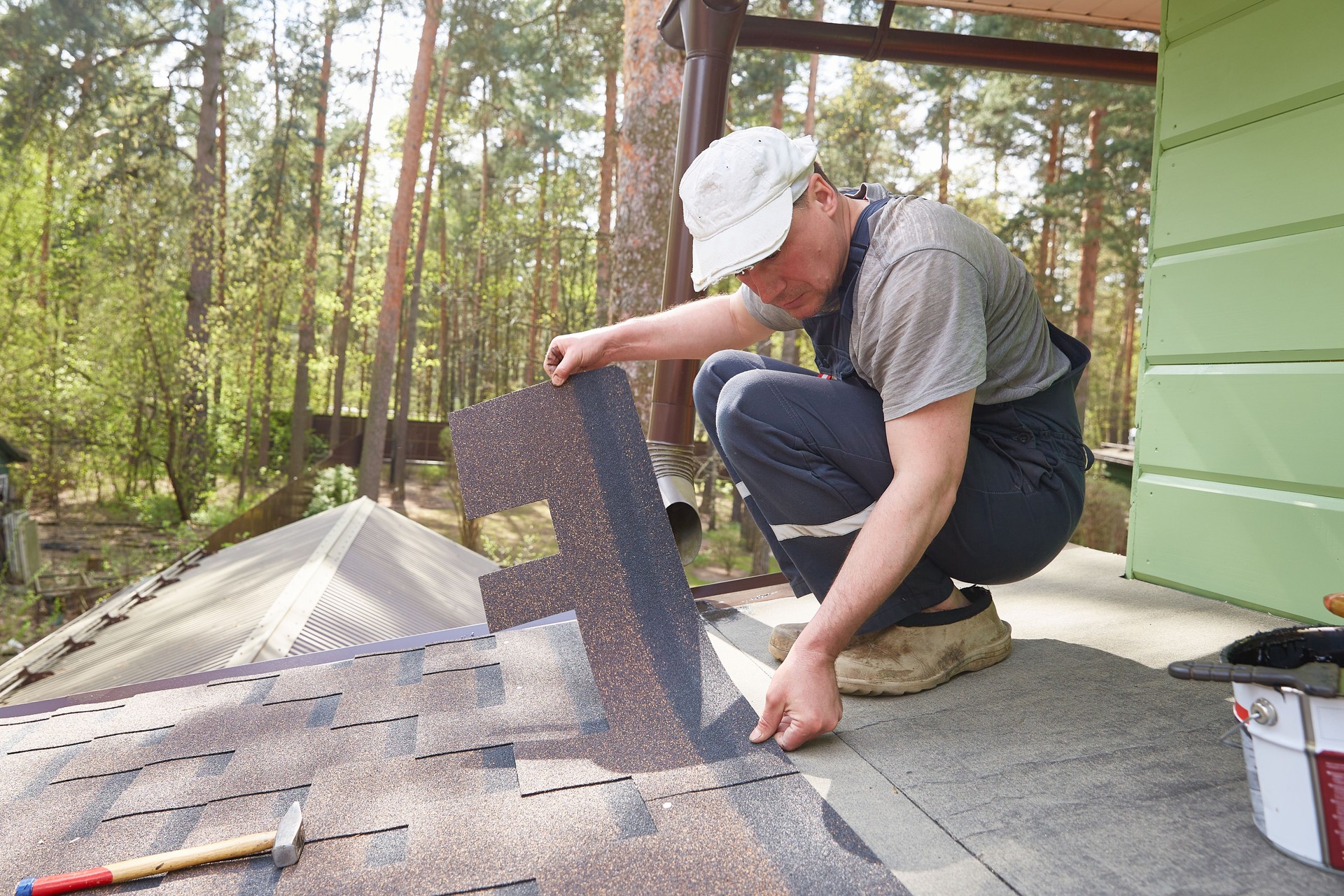 A man lays a roof of soft tiles on the roof of a country house.